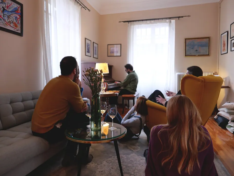 Guests on a sofa and armchairs listen to a solo piano recital by lamplight