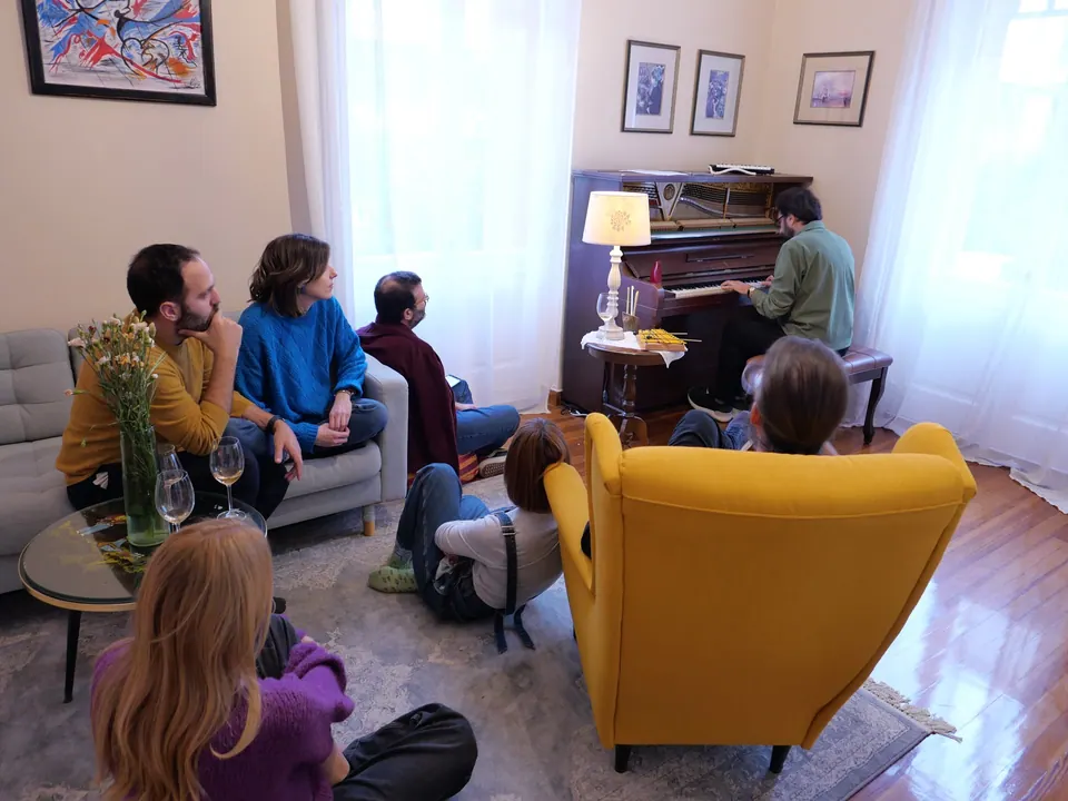 The living room from above, with the open upright piano and guests gathered around it