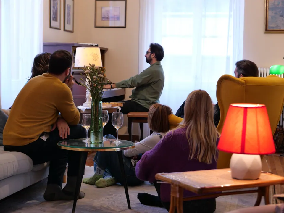 The pianist plays while guests listen beside a red table lamp
