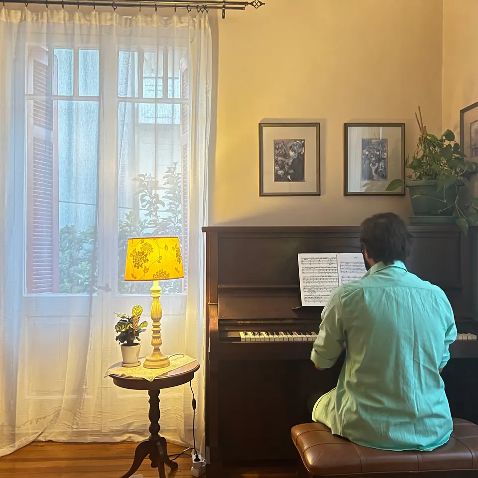 The pianist at the upright piano, beside a tall window and a yellow lamp